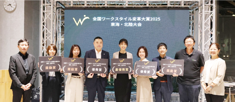 表彰式で登壇者と並ぶ、情報・コミュケーション企画部長の川瀬 直樹（左から4人目）